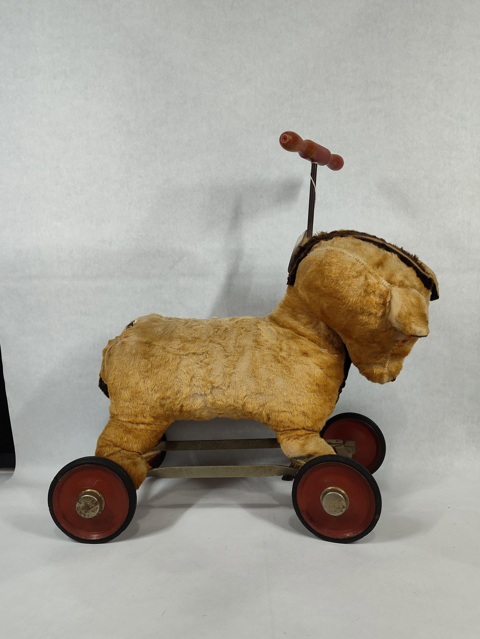 Vintage Steerable Ride-On Donkey Toy: This vintage ride-on toy features a stuffed animal, designed in the form of a donkey, mounted on a metal frame. The body is constructed of tan plush material, likely mohair, over a rigid