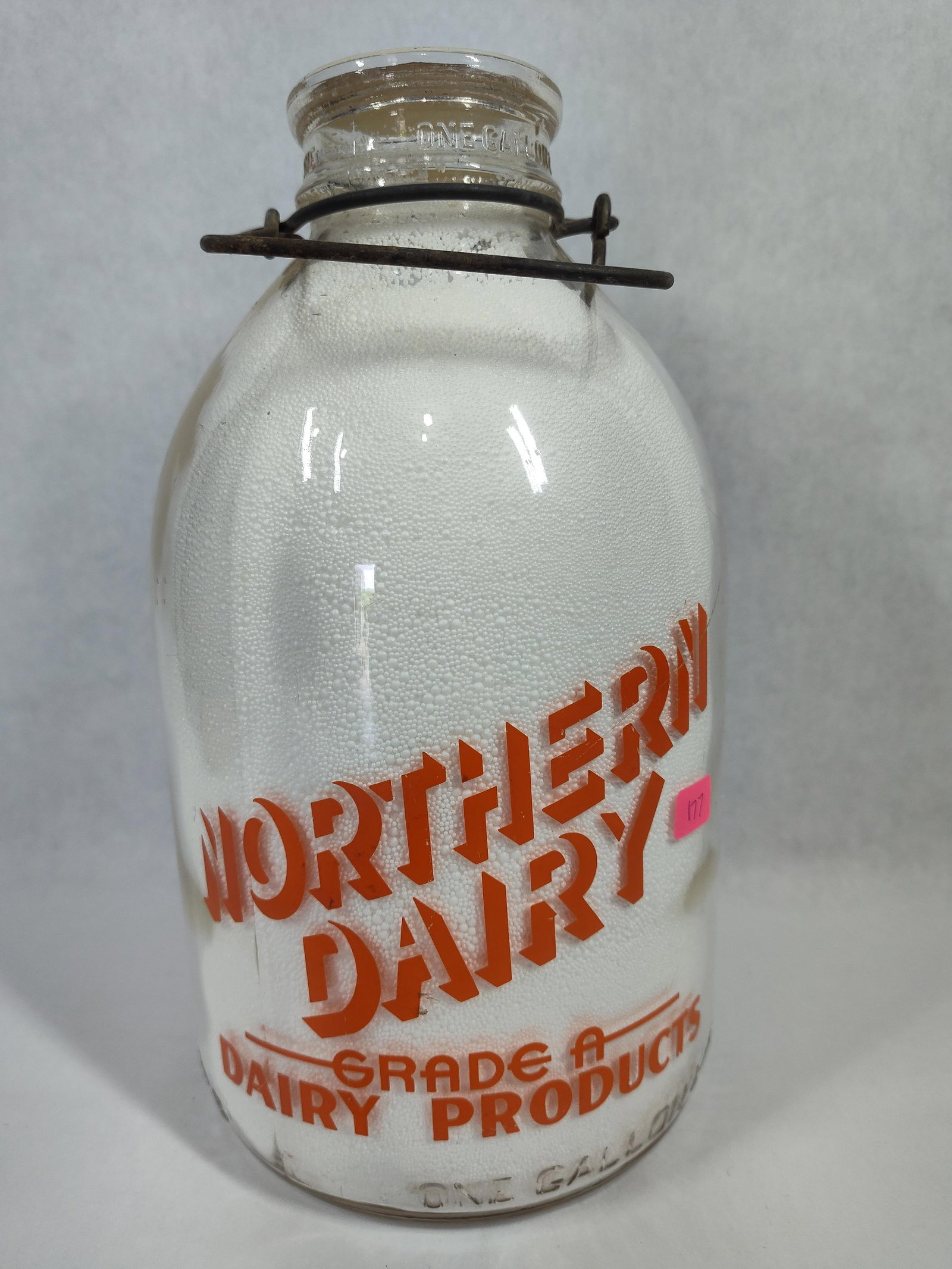 Vtg Northern Dairy Glass Milk Bottle w/ Wire Bale: This vintage one-gallon glass milk bottle is from Northern Dairy, located in Brighton, Colorado. The clear glass vessel features orange applied color labels (ACL) on two sides. The front face