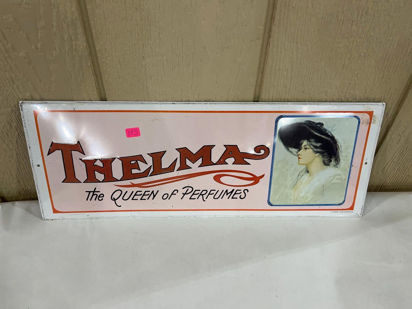 Sanford J. Heilner 1974 Thelma Perfume Tin Sign: This lithographed metal advertising sign is a 1974 reproduction of early 20th-century promotional materials for Thelma perfume. Produced by Sanford J. Heilner Inc. in the United States, the sign