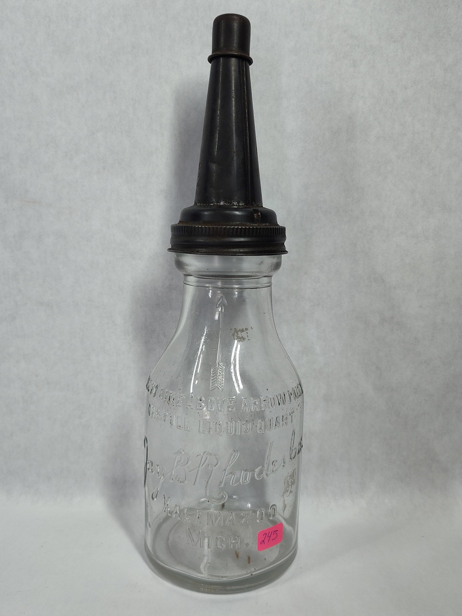 J.B. Rhodes Co. Oil Bottle w/ Master Spout: This antique petroliana item consists of a service station oil bottle and a dispensing spout. The bottle is constructed of clear molded glass and is embossed with the text Fill Line Above Arrow and