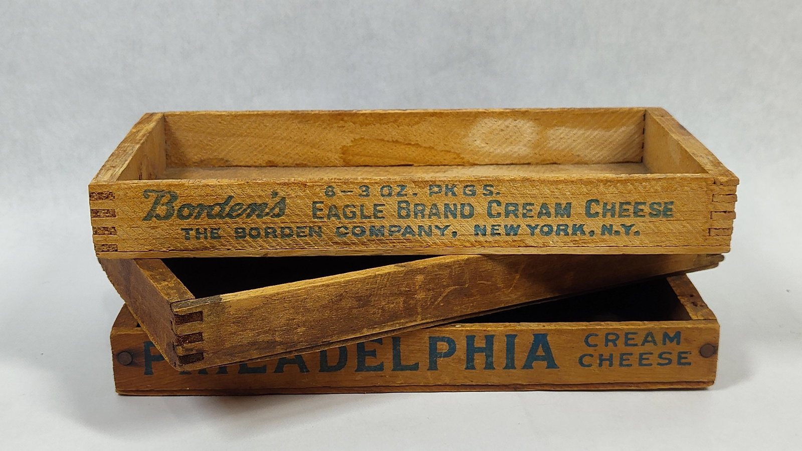 3 Vtg Borden's & Philadelphia Wood Cheese Crates: A trio of vintage wooden cheese crates intended for shipping and retail display. The collection consists of one Borden's Eagle Brand crate, one Philadelphia Cream Cheese crate, and one unmarked