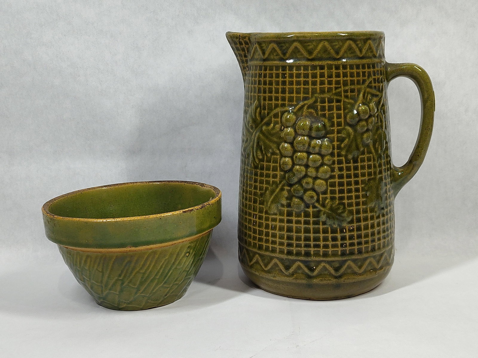 2 American Green Earthenware Grapes & Lattice Pcs: This lot features two pieces of American molded earthenware pottery finished in a mottled green glaze. The primary item is a large pitcher decorated with a Grape and Lattice relief pattern,