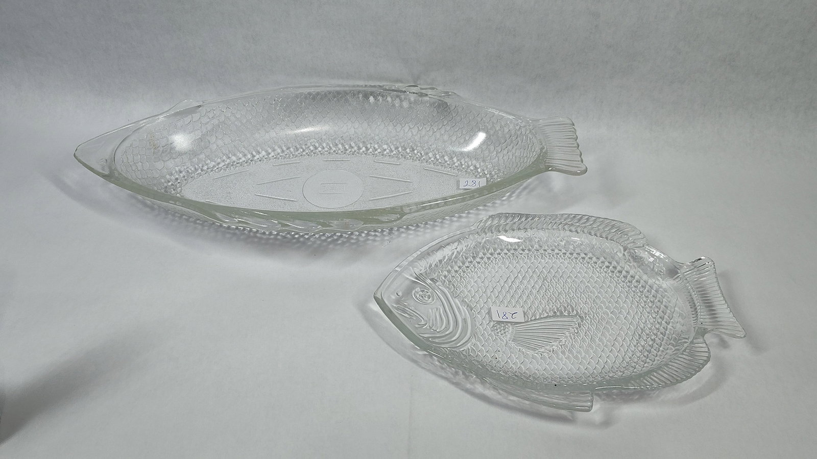 Pair Glasbake & Fish-Shaped Glass Serving Dishes: A two-piece set of clear pressed glass serving dishes, both featuring a fish motif. The collection consists of one large oval serving bowl and one smaller shallow serving plate. The large bowl is mark