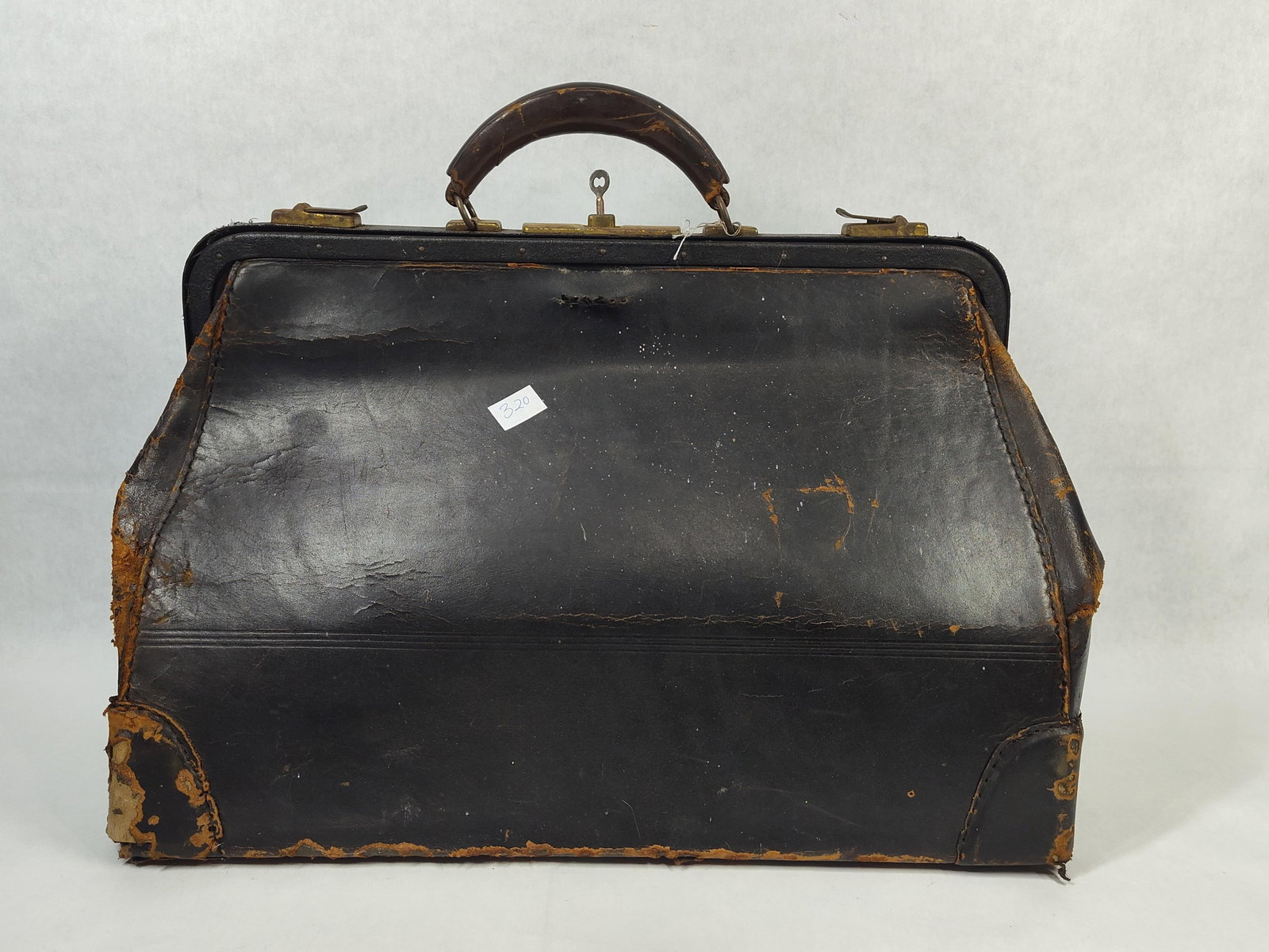 Black Leather Gladstone Style Medical Doctor Bag: This antique Gladstone-style bag is constructed of black leather over a hinged metal frame, typically used as a medical doctor's bag or for travel. The exterior features a single leather-wrapped