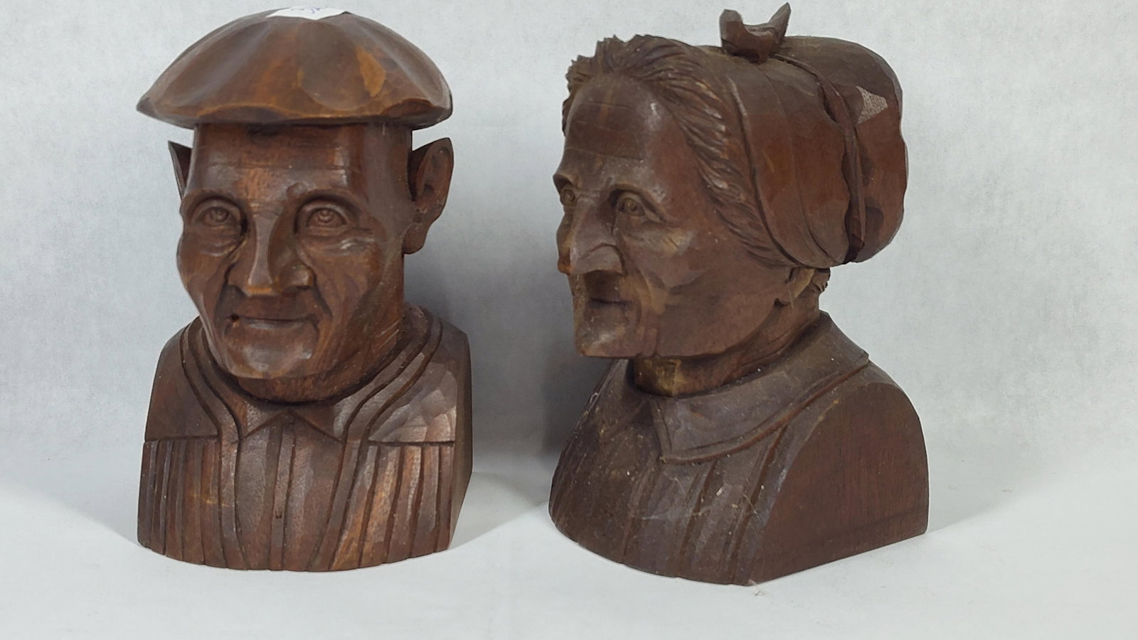 Pair Wood Busts of an Elderly Couple: A pair of hand-carved wooden busts depicting an elderly man and woman, rendered in the style of European folk art or Anri-style carvings. Each figure is depicted from the chest up and features
