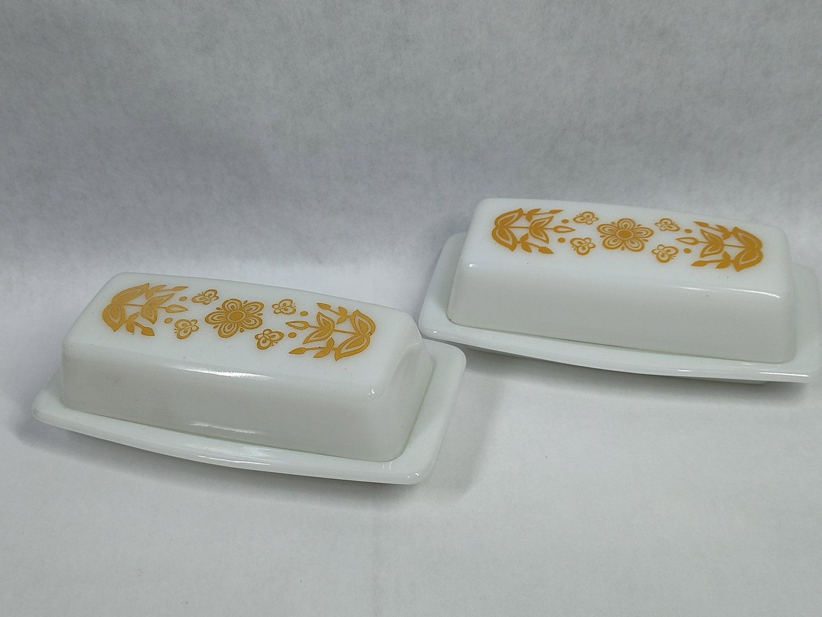Pair Pyrex Butterfly Gold Covered Butter Dishes: This lot features a pair of vintage milk glass covered butter dishes produced by Pyrex (Corning Glass Works). Both items are decorated with the Butterfly Gold pattern, a popular mustard-yellow silk-sc