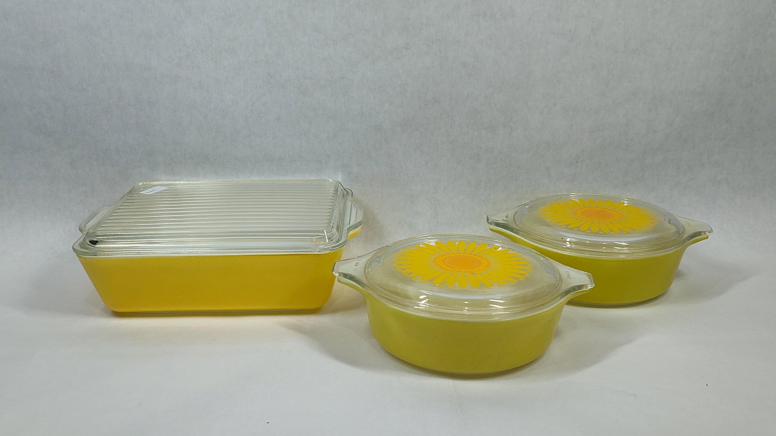 Trio Pyrex Daisy Pattern Yellow Glass Casseroles: This set of three vintage Pyrex ovenware items features the Daisy pattern, also known as Sunflower, which was introduced in the late 1960s. The collection consists of one rectangular baking dish and t