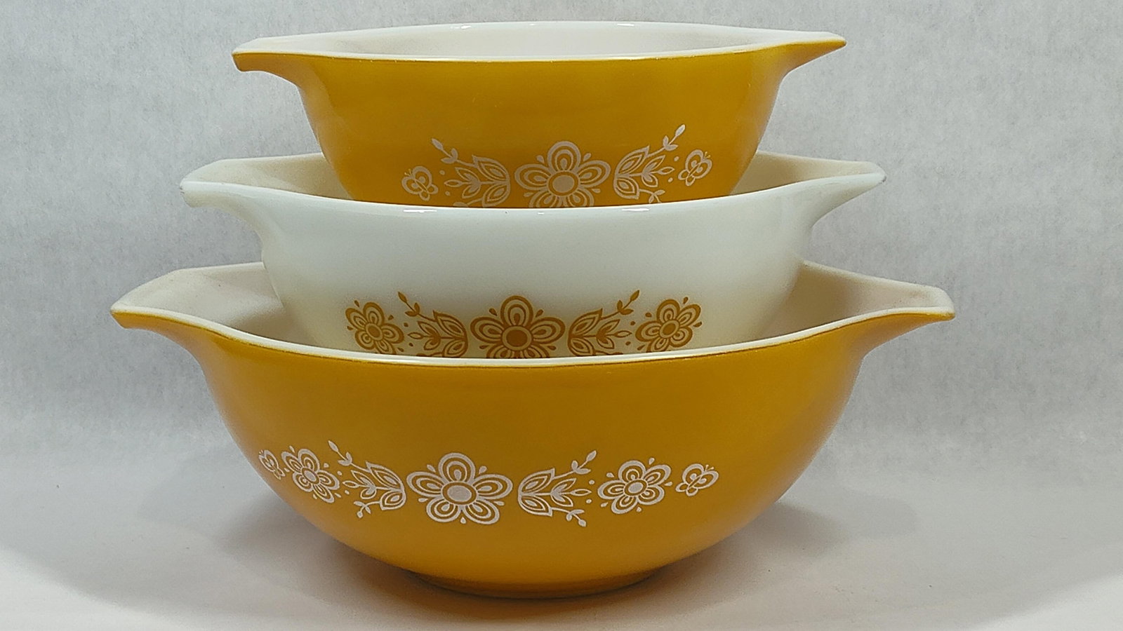 Vtg Pyrex Butterfly Gold Cinderella Nesting Bowls: A trio of vintage Pyrex Cinderella style nesting mixing bowls in the Butterfly Gold pattern, Version 1. These bowls are constructed of tempered opal glass, commonly known as milk glass. The Cinderella