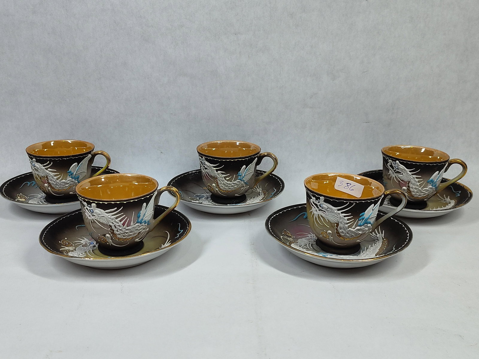 5 Japanese Moriage Dragonware Porc. Cups & Saucers: A set of porcelain teacups and matching saucers featuring traditional dragonware decoration. Each piece displays hand-applied moriage, or raised slip, forming a three-dimensional dragon design in