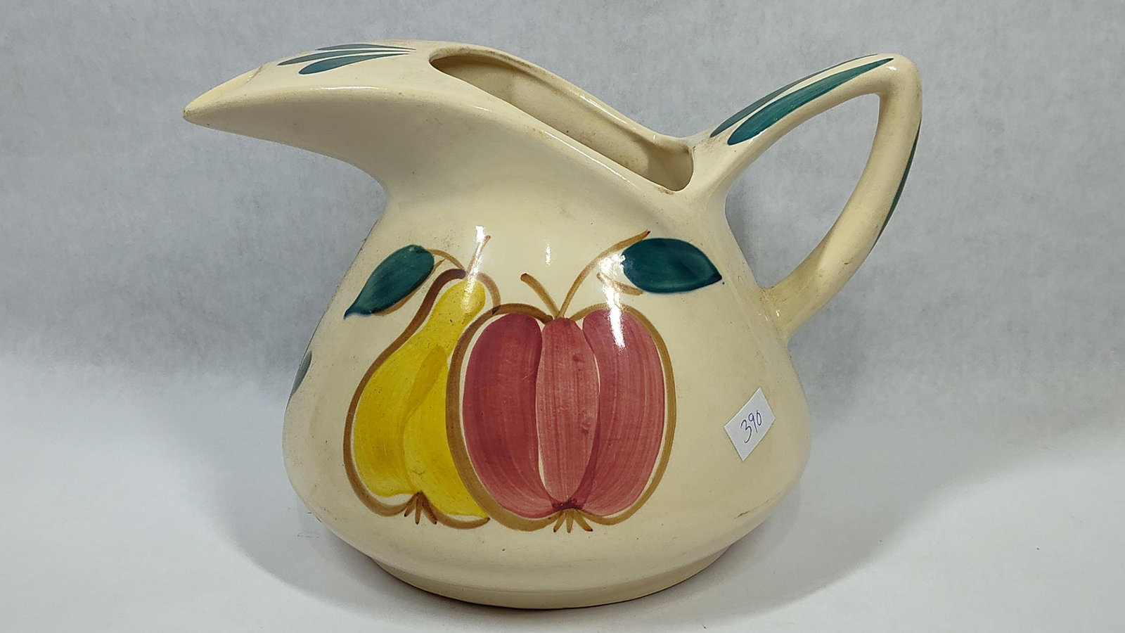 Purinton Pottery Apple & Pear Ice Lip Pitcher: A vintage ceramic pitcher manufactured by Purinton Pottery. The vessel is constructed from earthenware with a cream-colored ground and a clear glaze. It features a bulbous, low-slung body and a