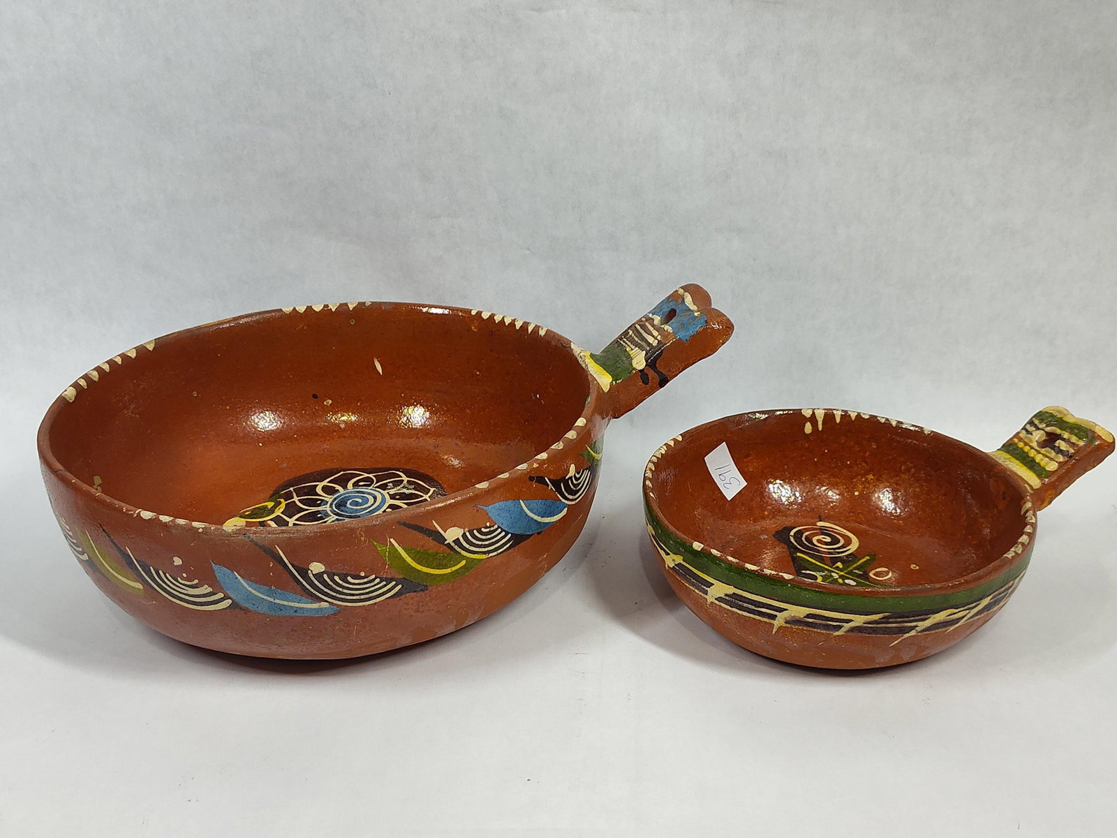 Pair Tlaquepaque Mexican Terracotta Hanging Bowls: This pair of Mexican folk art pottery bowls, known as cazuelas, originates from the renowned ceramic center of San Pedro Tlaquepaque in Jalisco. The lot consists of two shallow earthenware vessels of