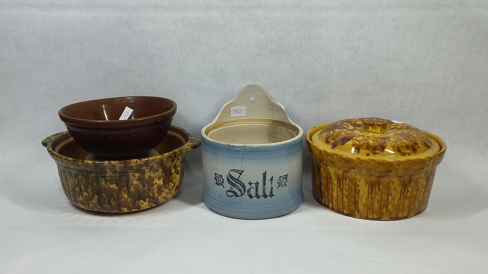 American Utilitarian Stoneware & Yellowware: This collection features an assortment of late 19th to early 20th-century American utilitarian pottery. The group includes a shaded blue and white glazed stoneware salt crock with an arched backplate