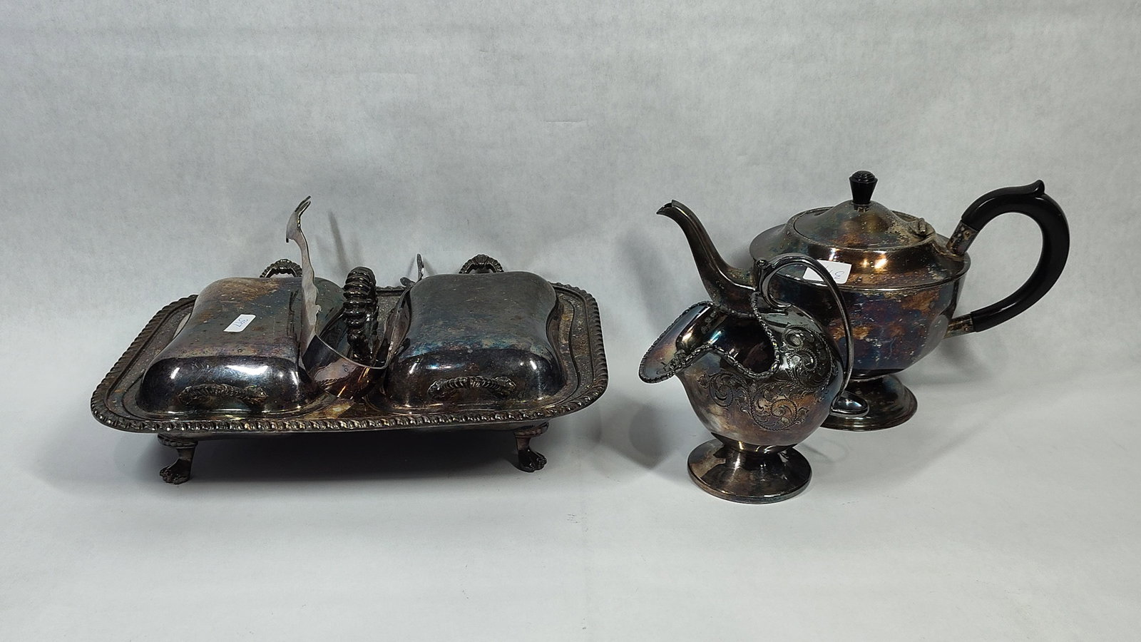 Silver-Plated Teapot, Sugar Scuttle & Entree Dish: A trio of silver-plated table items comprising a teapot, a sugar scuttle, and a double entree dish. The teapot is designed with a faceted body on a flared circular foot, featuring an ebonized