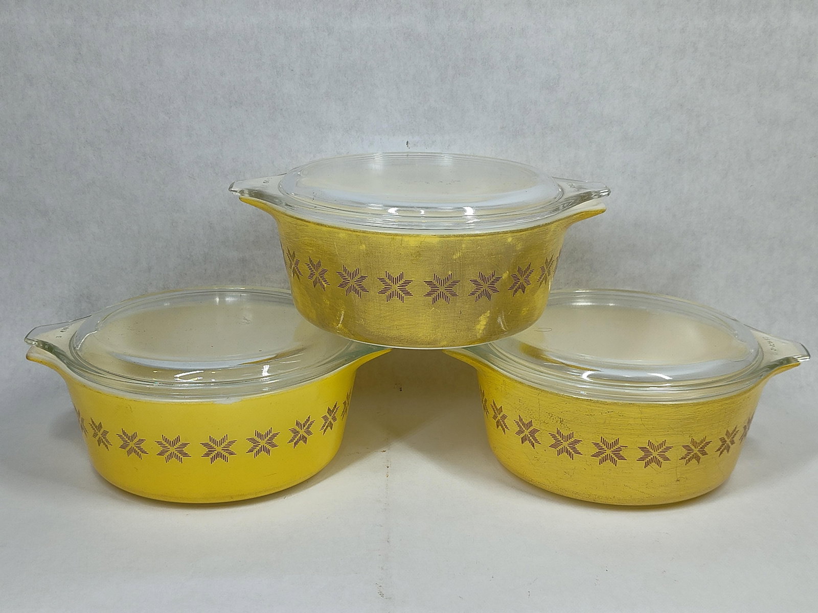 Pyrex Town & Country Covered Casseroles, Trio: A trio of vintage Pyrex round casserole dishes accompanied by clear glass lids. These pieces feature the Town and Country pattern, consisting of a repeating horizontal band of stylized brown star or s