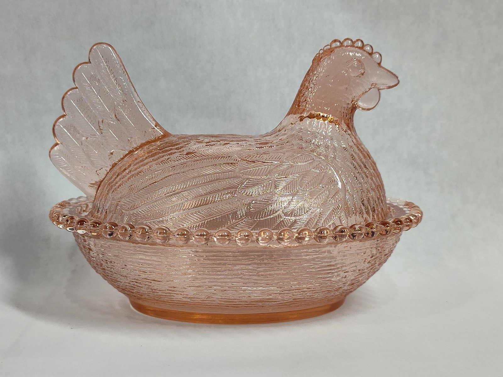 Indiana Glass Pink Pressed Glass Hen on Nest Dish: This two-piece covered decorative dish is fashioned in the classic hen on nest form. The item is constructed from translucent pink pressed glass. The top section consists of a lid molded to resemble