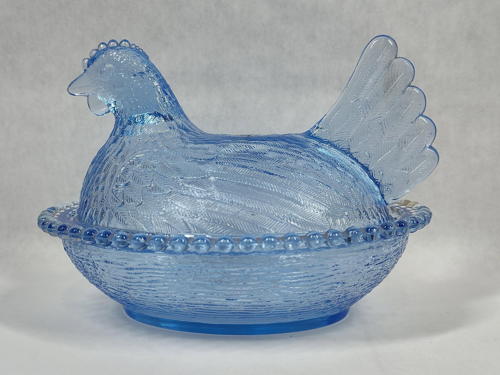 Boyd Crystal Art Glass Light Blue Hen on Nest Dish: This is a pressed glass Hen on Nest covered dish produced by Boyd Crystal Art Glass of Cambridge, Ohio. The piece consists of two parts: a lid in the form of a nesting hen and a base shaped like a