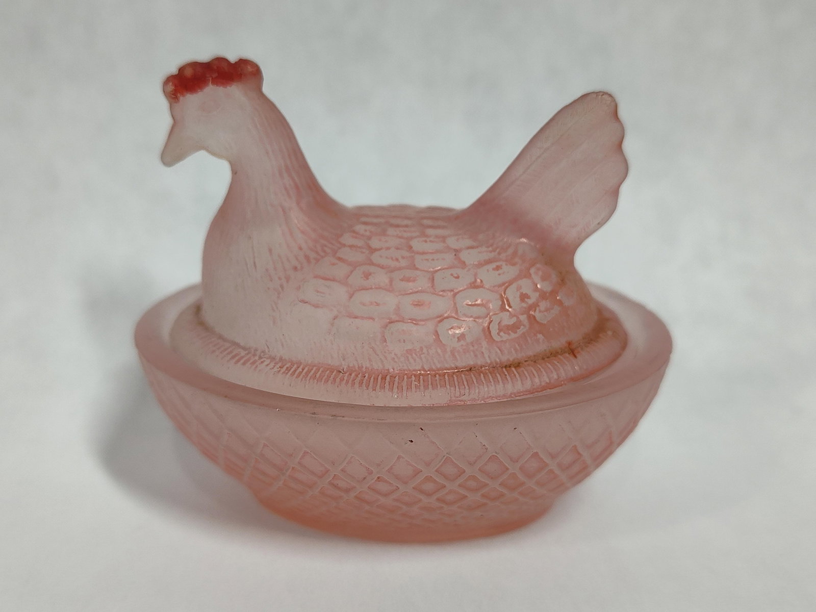 Pink Satin Glass Hen on Nest Covered Dish: A pink satin glass covered dish consisting of a lid in the form of a hen and a matching basketweave patterned base. The piece features a frosted matte finish throughout. The lid is molded into the