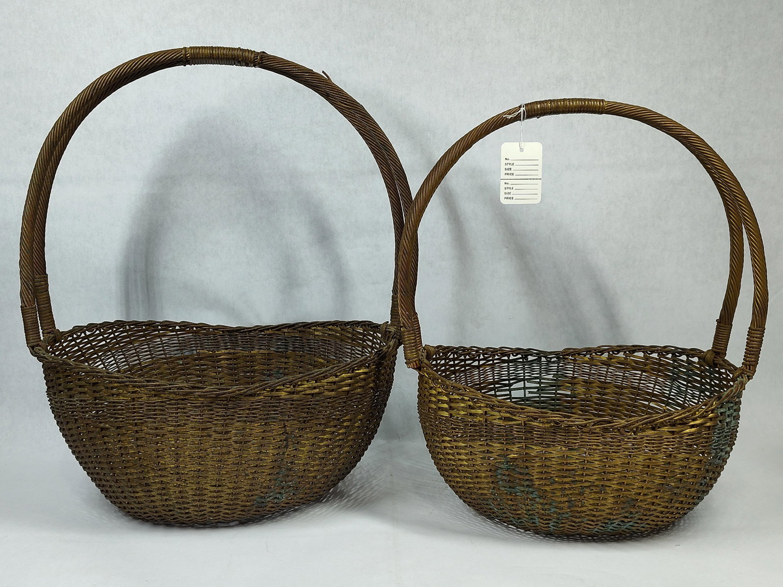 Pair Mid-Century Woven Brass Wire Baskets: A pair of vintage decorative baskets constructed from woven brass wire. Each basket features a rounded bowl with a dense wire-weave body and a central square-woven structural pattern at the base. The