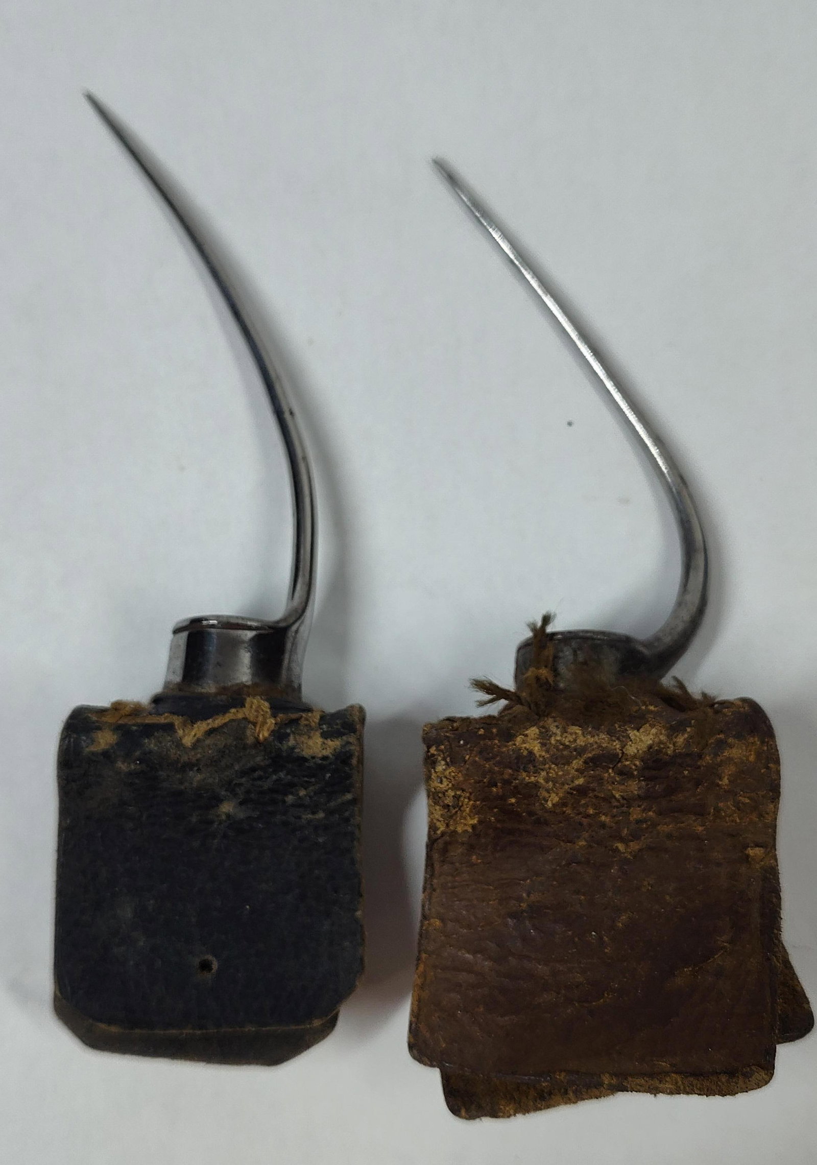 A Pair of Antique Cockfighting Gaffs: A pair of antique cockfighting gaffs, also known as spurs, designed for use in gamecock competitions. Each item consists of a long, slender, curved steel needle with a sharp point, mounted to a small 