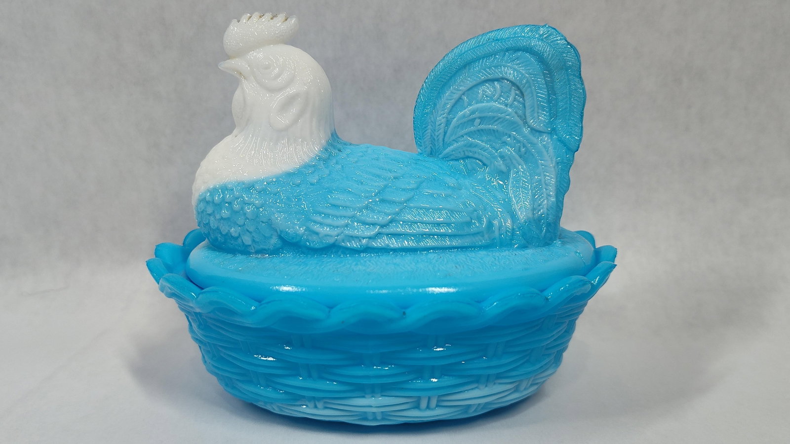 Blue and White Slag Glass Rooster on Nest Covered Dish: This two-piece pressed slag milk glass covered dish is designed in the form of a rooster on a nest and is attributed to the Westmoreland Specialty Glass Company. The item is crafted from opaque slag g