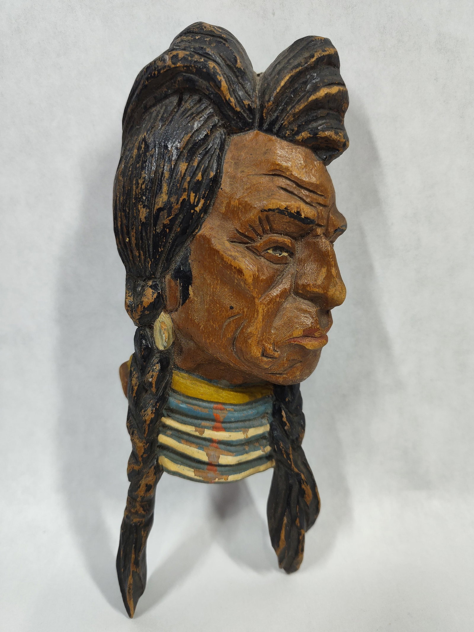 Native American Polychrome Wood Bust Wall Plaque: This hand-carved wooden wall plaque depicts the profile of a Native American man. The figure is rendered with expressive facial features, including deep-set lines and a prominent brow. The subject is 