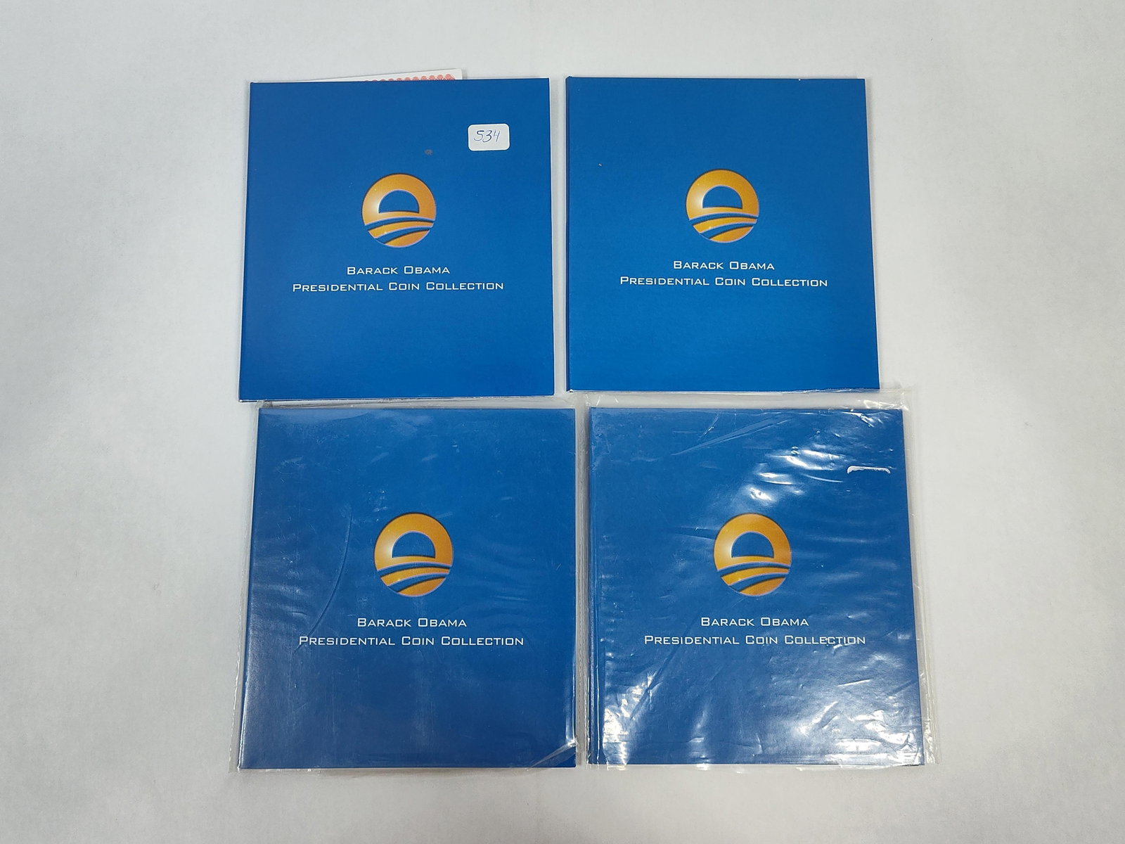 4 U.S. Coin Network Barack Obama Presidential Sets: A lot of four Barack Obama Presidential Coin Collection sets, produced and distributed by the U.S. Coin Network. Each set is housed in a gatefold blue cardstock display folder featuring a stylized
