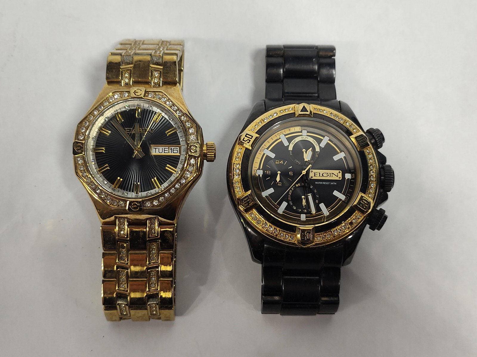 Pair Elgin Men's Wristwatches FG160056ST/FG160064: This lot features two modern Elgin quartz wristwatches with decorative crystal accents. The first timepiece, reference FG160056ST, has a gold-tone base metal case and an octagonal bezel embellished