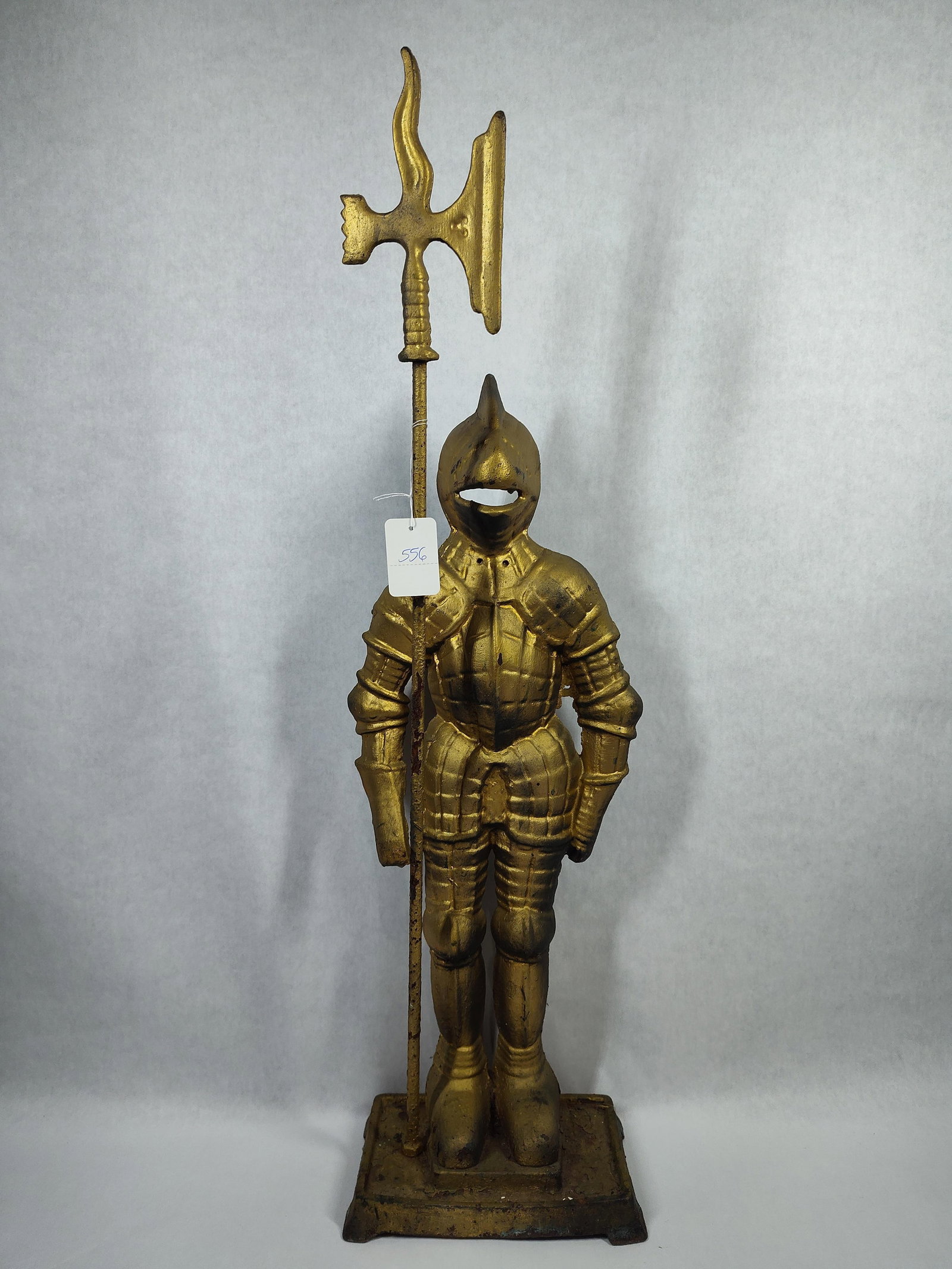 Vtg Cast Iron Knight in Armor Fireplace Companion: A decorative hollow-back figure of a knight in full plate armor, standing on a rectangular plinth. The knight is depicted in a formal standing pose, holding a long-poled halberd. The armor is styled
