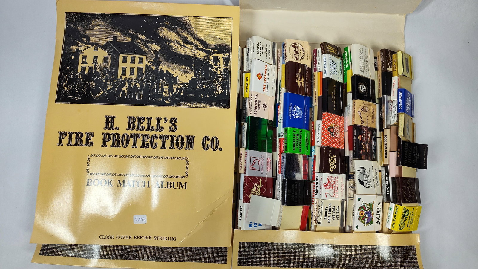 H. Bell's Fire Protection Co. Matchbook Collection: A collection of vintage advertising matchbooks housed in an H. Bell's Fire Protection Co. Book Match Album produced by Bandwagon Inc. The album is constructed of tan cardstock and features a black