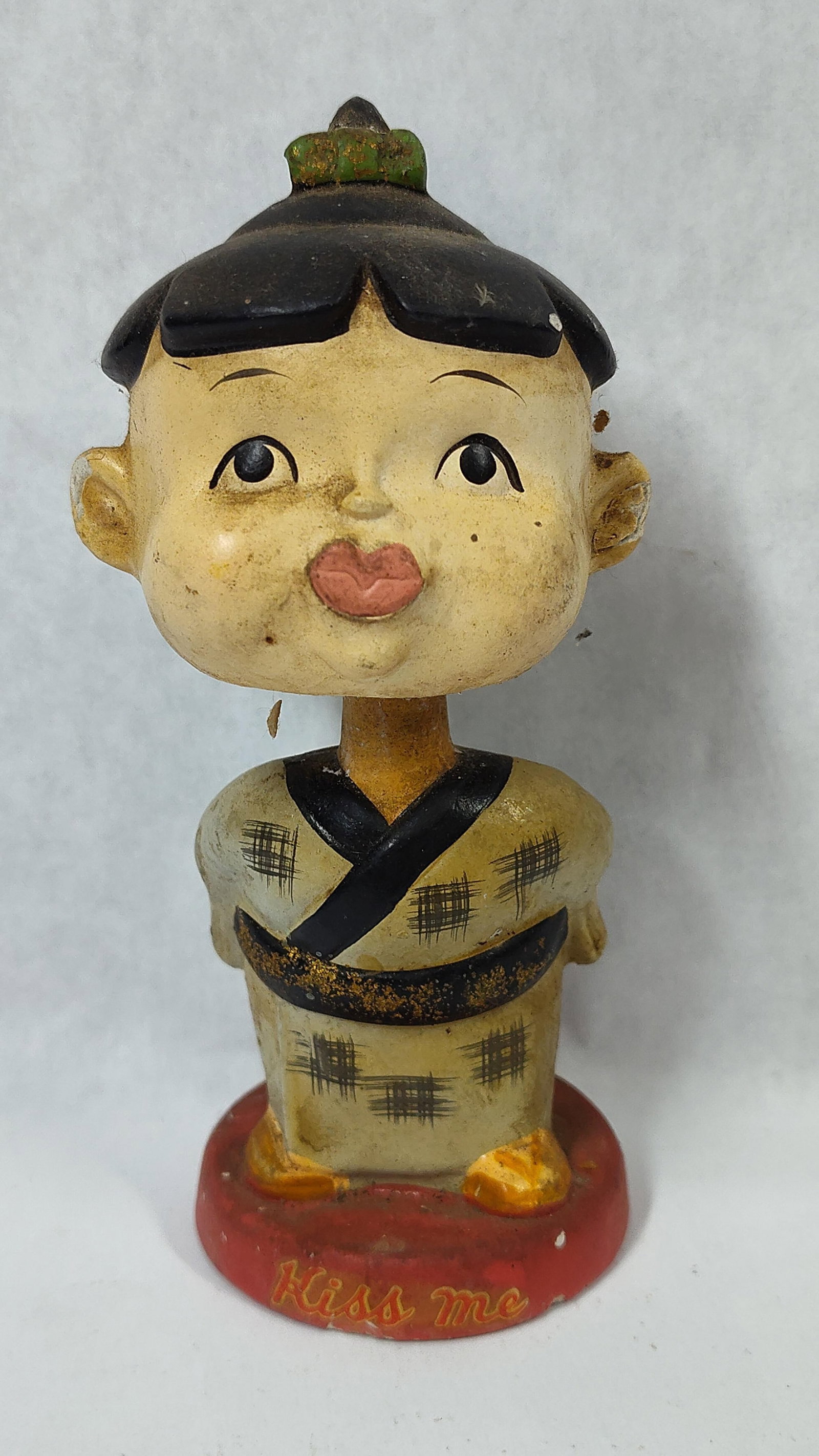 Lego Chalkware Asian Child Kissing Nodder, Japan: A mid-20th century hand-painted chalkware nodder figurine imported by Lego. The figure portrays a child in traditional Japanese attire, specifically a grey-toned kimono decorated with black checkered