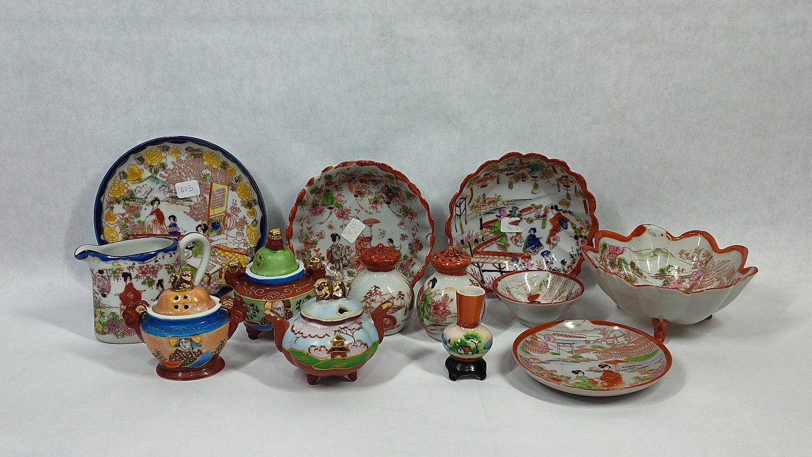 13 Japanese Geisha Girl Porc. & Earthenware: A collection of thirteen Japanese Geisha Girl pattern ceramics manufactured for the export market. The assortment is composed of porcelain and fine earthenware forms, including a creamer with a