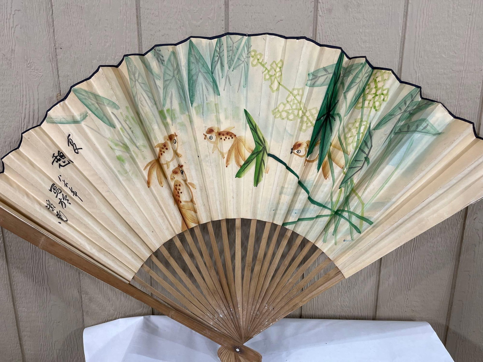 Lingnan School Chinese Goldfish Folding Fan, 1986: This Chinese folding fan features a watercolor and ink painting on a paper leaf, depicting four goldfish swimming among green aquatic foliage and small yellow blossoms. The artwork is executed in a