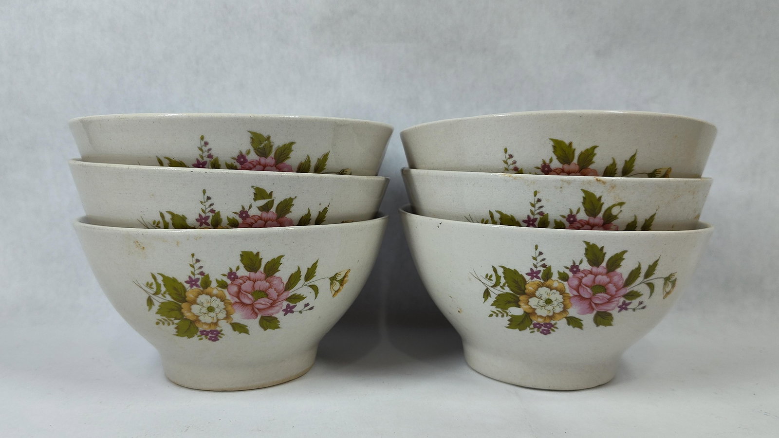 Set 6 Footed Ceramic Bowls w/ Floral Transfer: This set of six footed ceramic bowls is constructed from an off-white earthenware or semi-porcelain. Each bowl features a tapered form supported by a short pedestal foot. The exterior of each vessel