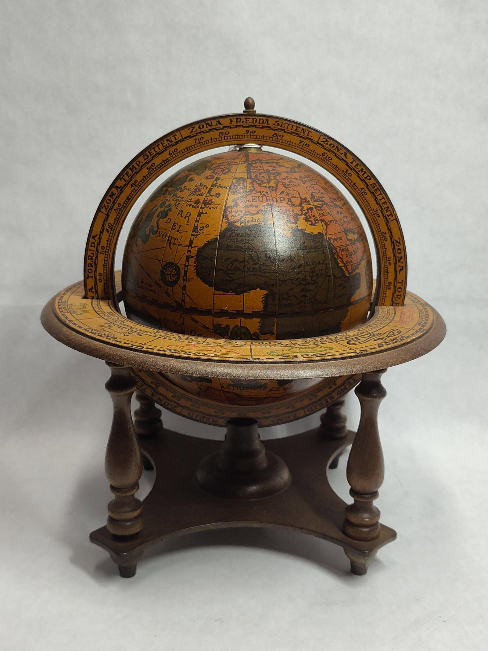 Italian-Style Wooden Globe w/ Zodiac Horizon: This item is a decorative tabletop globe featuring a reproduction map in the style of 16th-century Italian cartography. The globe is constructed with printed paper overlays on a composite sphere, moun