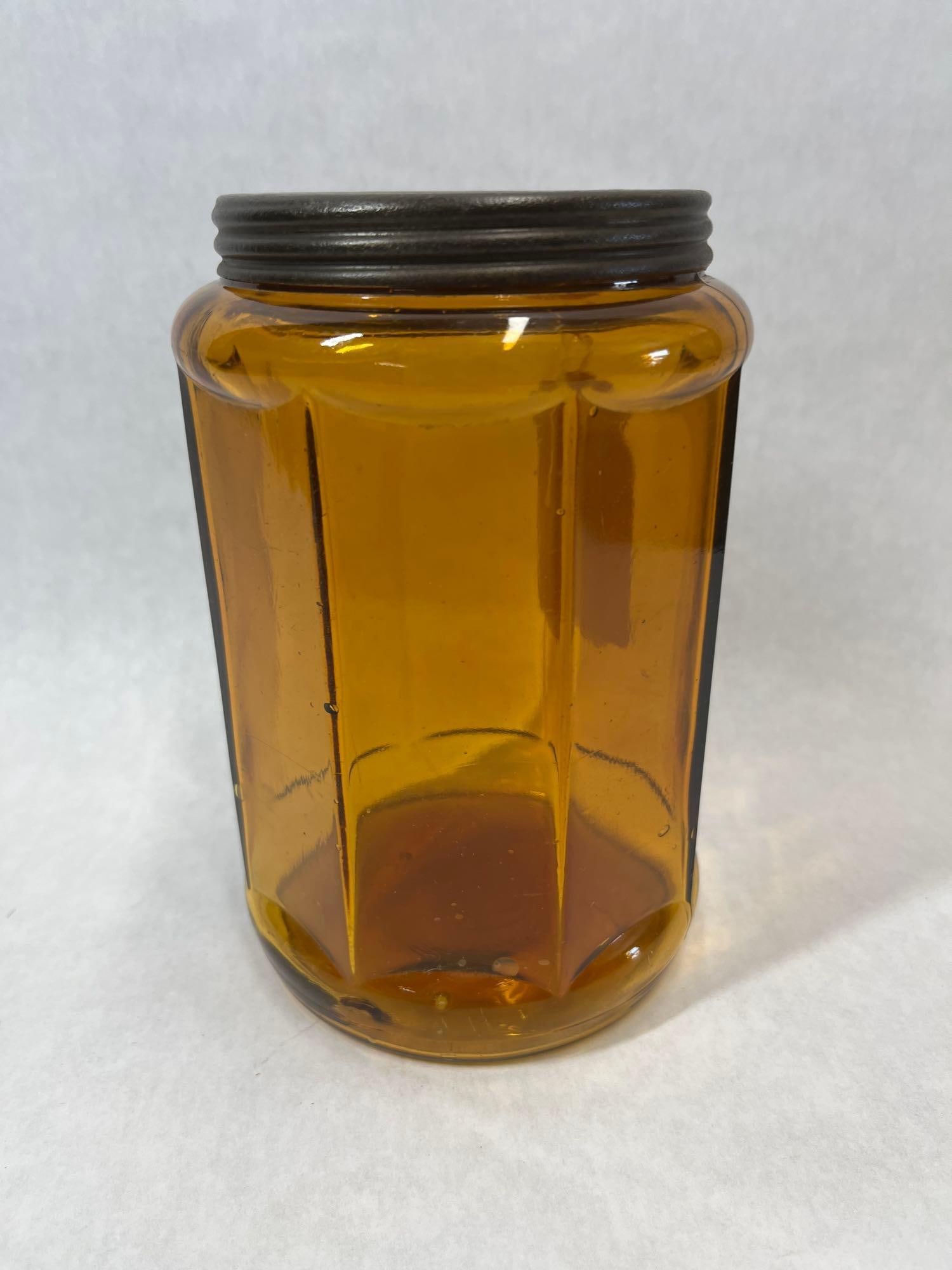 Mid-20th C. Amber Faceted Glass Jar w/ Metal Lid: A mid-20th-century amber pressed glass storage jar of American origin. The jar is constructed with a decagonal, ten-sided paneled body featuring faceted sides that taper slightly toward the base. It h
