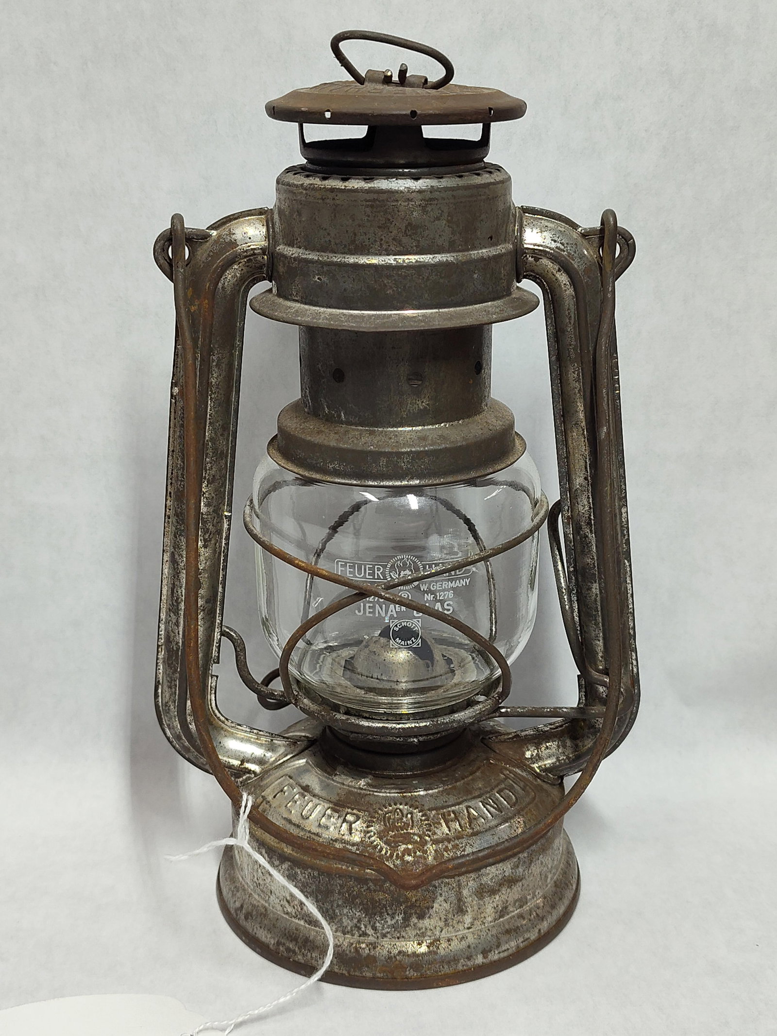 Nier Feuerhand No. 275 Baby Hurricane Lantern: A Nier Feuerhand No. 275 Baby model hurricane-style kerosene lantern featuring a steel body and glass chimney. The chimney cap is embossed with ORIGINAL - NIER FEUERHAND. The fuel tank is embossed