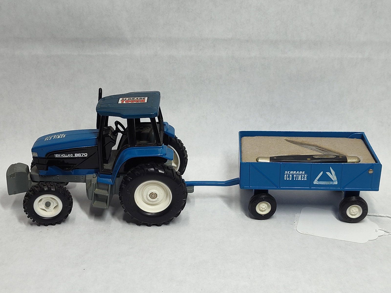 Ertl New Holland 8670 Tractor Set w/ Schrade Knife: This collectible promotional set, manufactured by Ertl for Schrade, features a New Holland 8670 model tractor and a matching trailer housing a serialized pocket knife. The tractor is constructed from