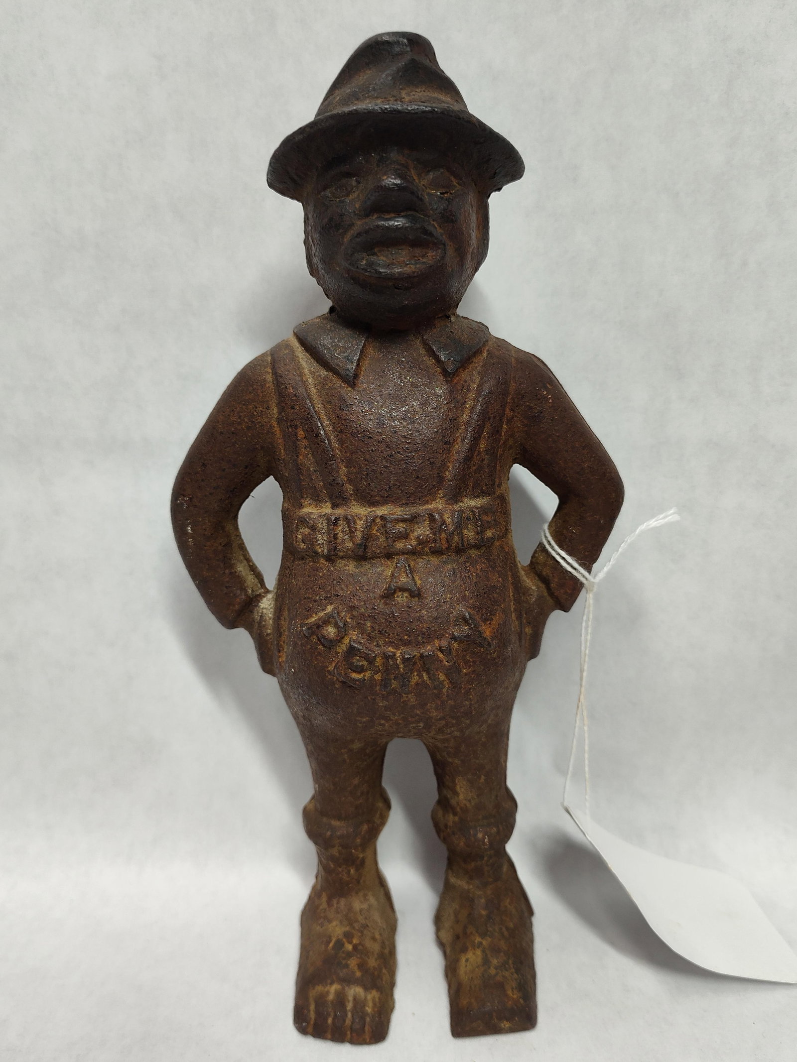 Give Me A Penny Still Bank: This still bank is designed in the style of early 20th-century American cast iron novelties. The figure depicts a caricatured man in a standing pose with hands placed on his hips, wearing a
