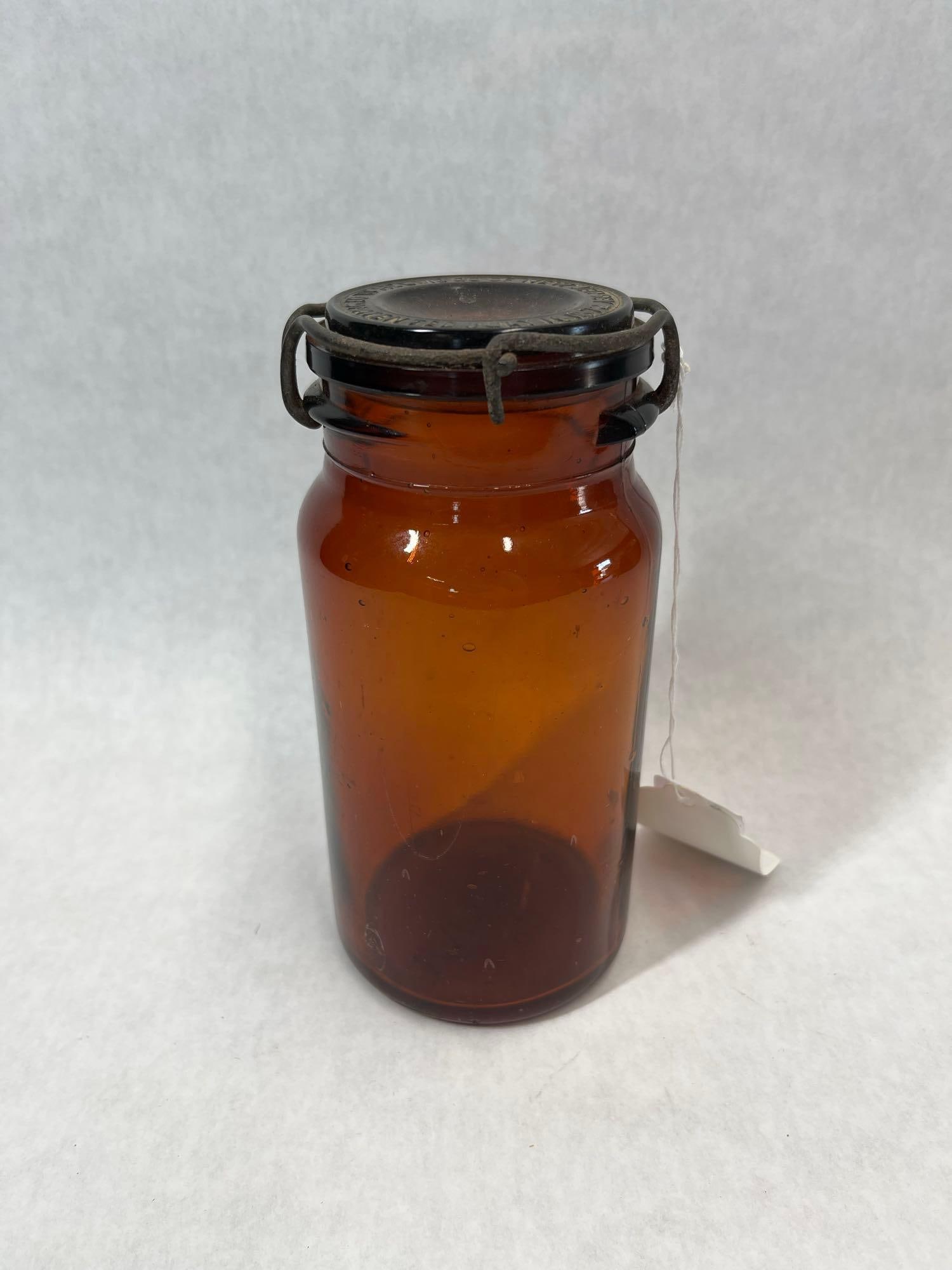 G.W. Helme & P. Lorillard Embossed Amber Snuff Jar: This antique snuff jar is constructed from deep amber glass and features a cylindrical body with a rounded shoulder. The jar is manufactured using a blown-in-mold technique, characterized by numerous