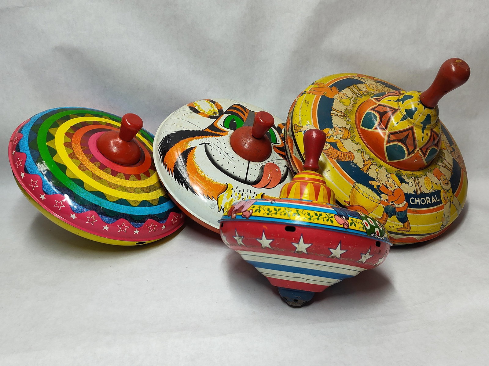 Wyandotte & Ohio Art 5 Tin Spinning Tops: This collection features five varied pump-action spinning tops constructed from lithographed tinplate. One top exhibits a geometric design in yellow, orange, and blue with a central metal spindle and