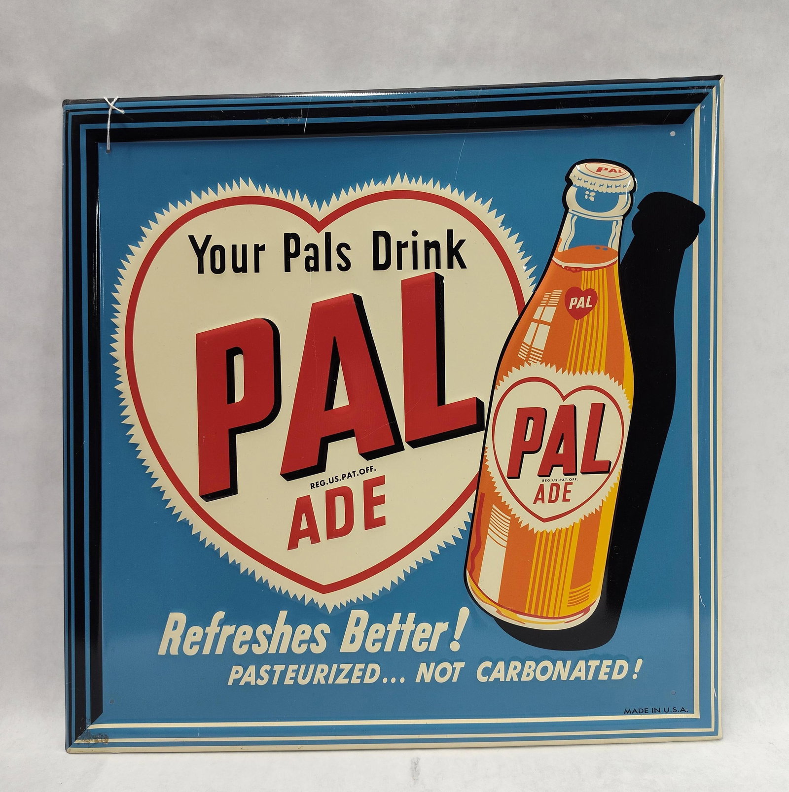 Pal-Ade Soda Embossed Metal Advertising Sign: A single-sided embossed metal advertising sign for Pal-Ade, a non-carbonated fruit beverage. The sign features a high-gloss finish over a vibrant blue background. At the center is a cream-colored