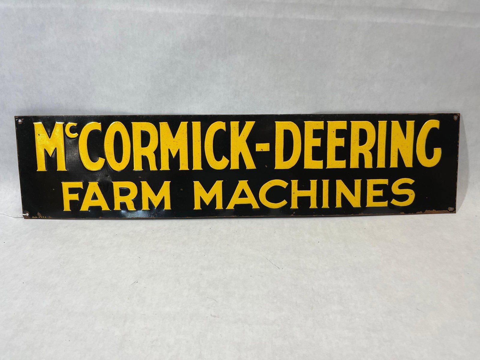 McCormick-Deering Farm Machines Metal Sign: An original embossed metal advertising sign for McCormick-Deering Farm Machines, a brand of the International Harvester Company. The rectangular sign features a black enameled background with