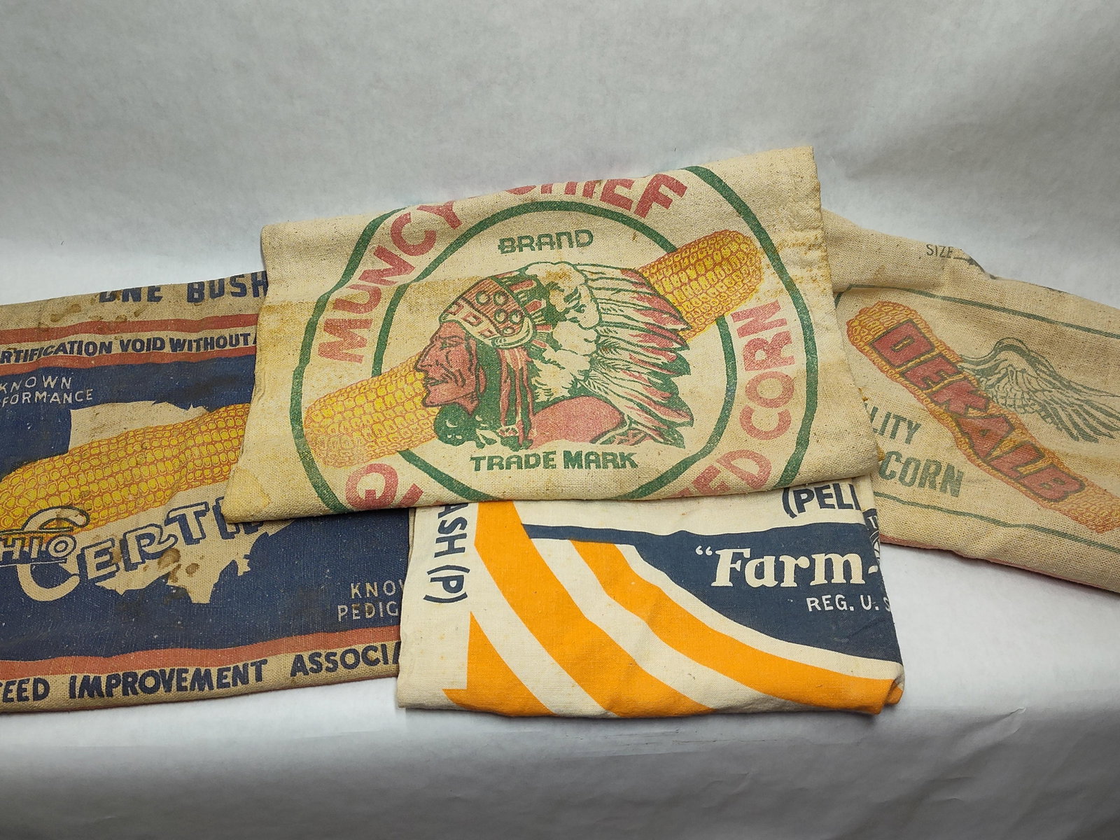 American Seed Corn & Poultry Feed Bags: This assortment features American agricultural advertising bags from the mid-20th century, primarily constructed of burlap and heavy cotton canvas. The collection includes a one-bushel Muncy-Chief