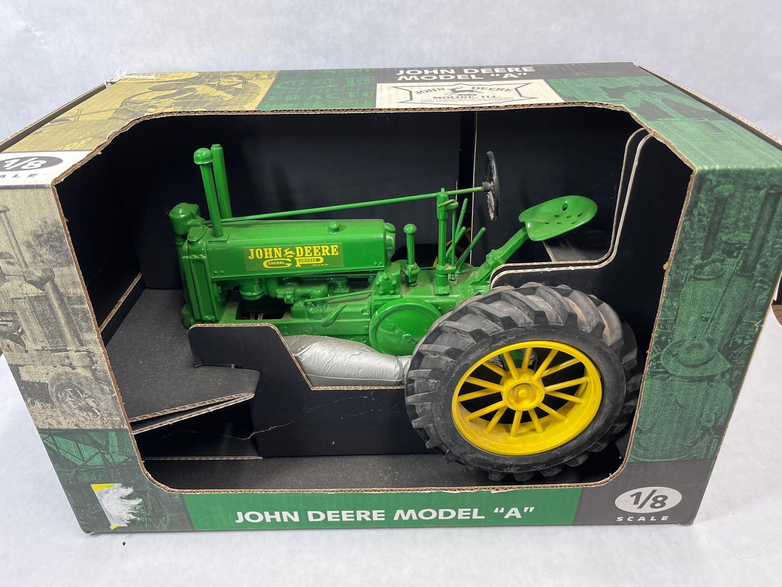 John Deere Model A 1/8 Die-Cast Tractor w/ Box: This 1/8 scale die-cast replica of a John Deere Model A tractor is presented in its original illustrated display box. Attributed to Ertl, the model features a highly detailed sand-cast metal body and
