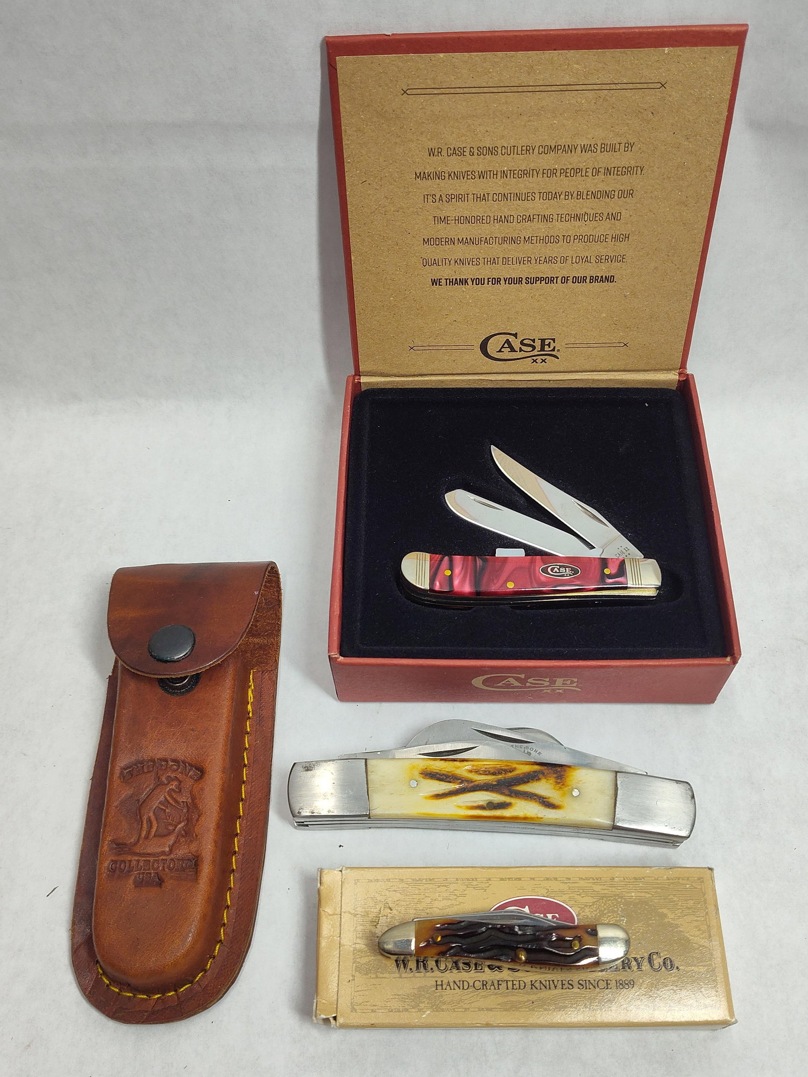W.R. Case & Sons Trio Folding Pocket Knives: This lot consists of three folding pocket knives produced by W.R. Case and Sons Cutlery Co. The first item is a Mini Trapper pattern featuring Cinnamon Swirl Kirinite synthetic handles. The blade tang