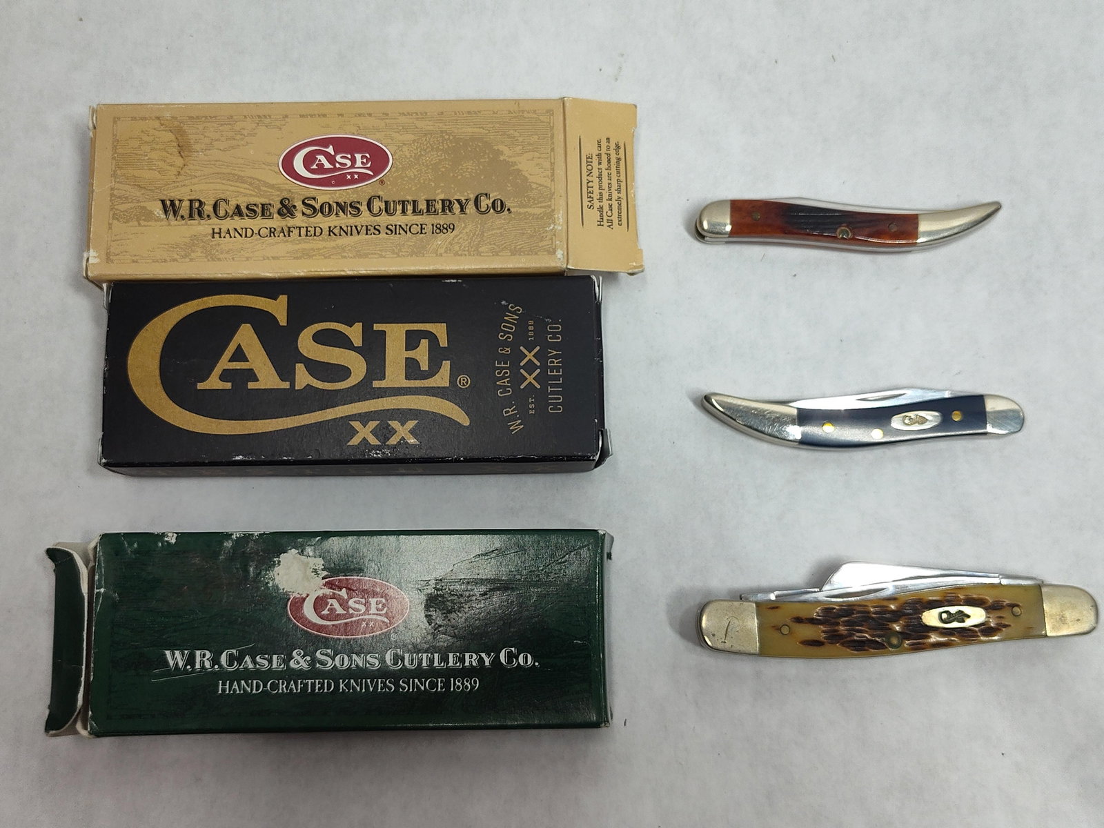 Trio W.R. Case & Sons Pocket Knives w/ Boxes: This lot consists of three folding pocket knives manufactured by W.R. Case & Sons Cutlery Co., each accompanied by its original manufacturer retail box. The first knife is a single-blade Tiny