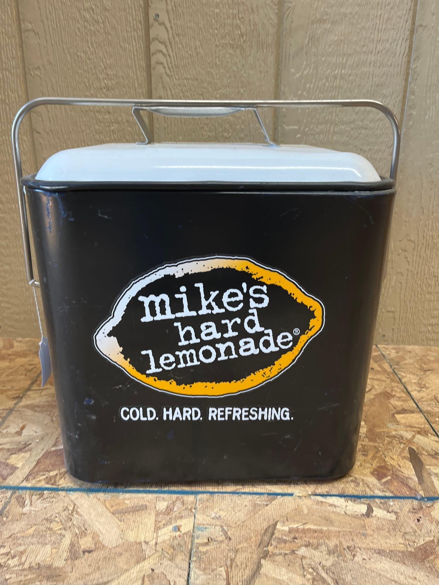 Mike's Hard Lemonade Cooler w/ Starr X Opener: A -style metal promotional picnic cooler produced for Mike's Hard Lemonade. The cooler features a black-painted metal body with a white lift-off lid. A large chrome-tone metal swing handle serves to