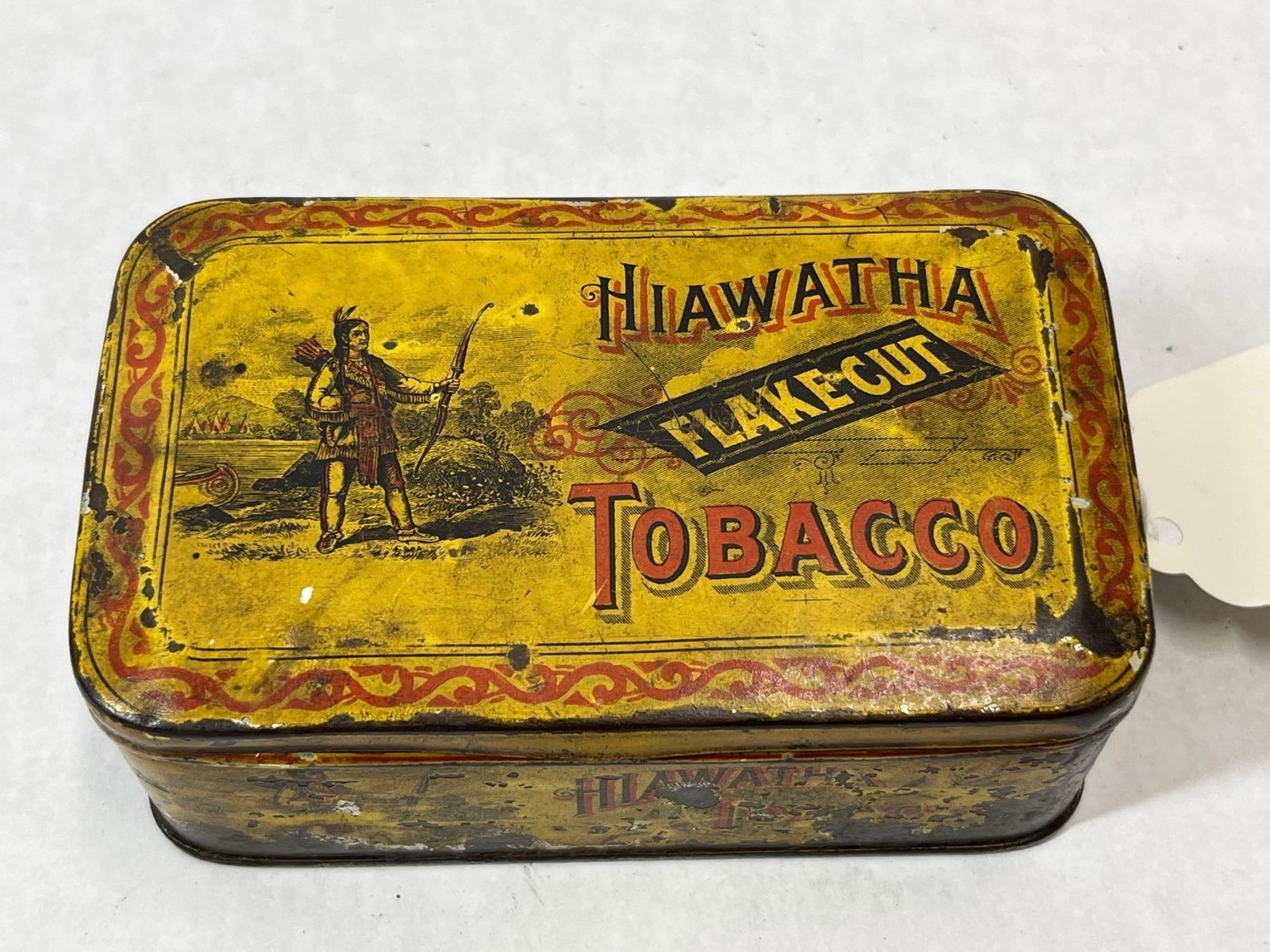 Daniel Scotten & Co. Hiawatha Lithographed Tin: An antique rectangular hinged-lid tobacco tin for Hiawatha Flake Cut Tobacco. The tin features a bright yellow lithographed ground. The lid is decorated with a central illustration of a standing