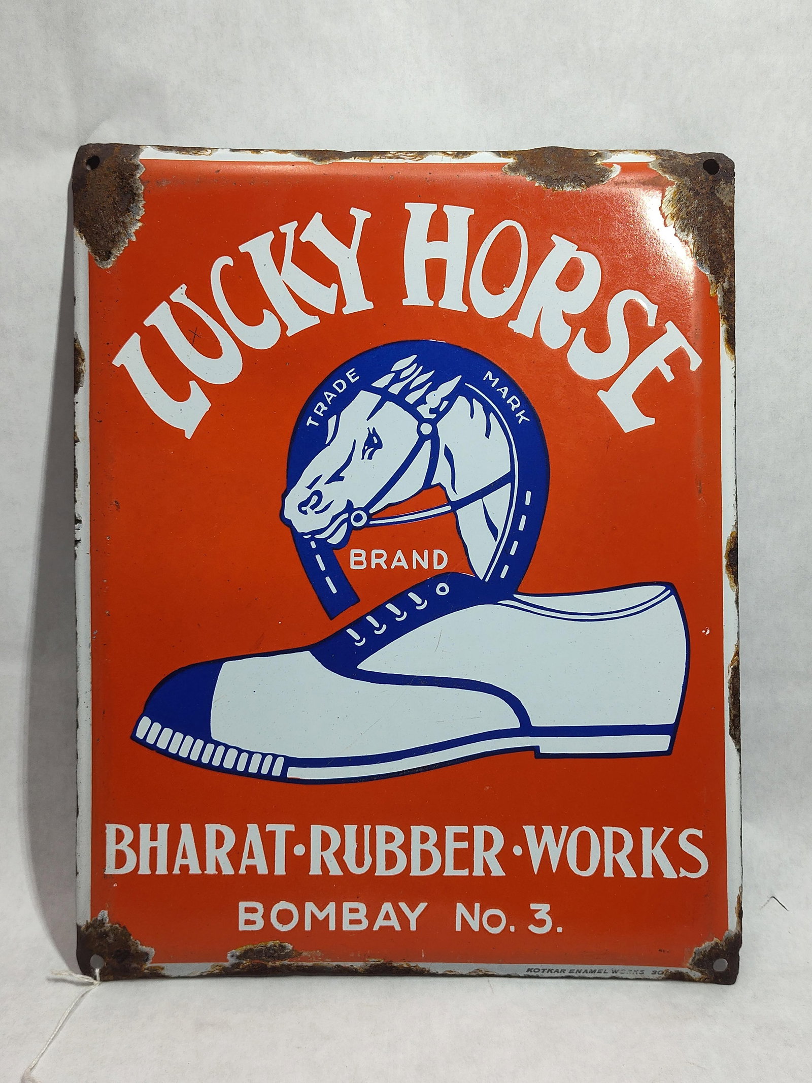 Lucky Horse Brand Bharat Rubber Porc. Enamel Sign: This rectangular advertising sign is made of vitreous enamel on a steel base, promoting Lucky Horse Brand shoes from Bharat Rubber Works. The sign features a bright orange field with white and blue