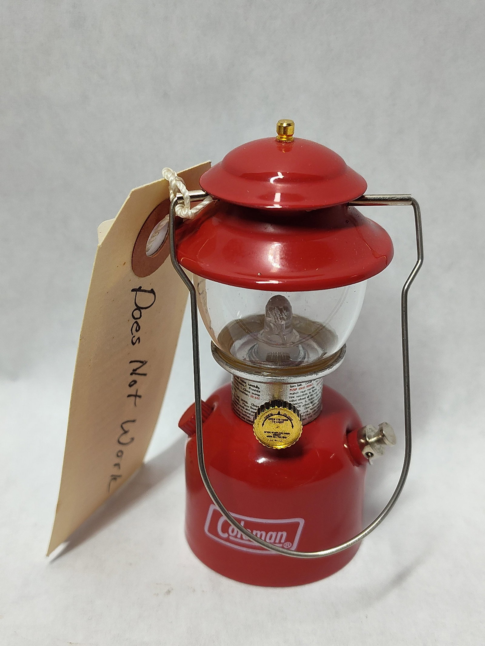 Miniature Coleman Model 200A Lantern Replica: This item is a miniature collectible lantern, designed as a scale replica of the Coleman Model 200A lantern. The piece features a red painted fount and ventilator top, a clear plastic globe, and a